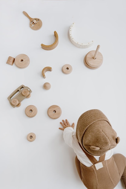 Top view of cute one year old baby in brown hat plays with stylish wooden toys Minimal baby fashion online shop online store concept