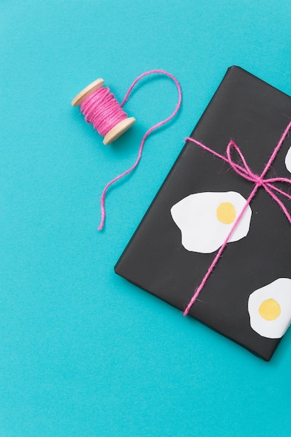 Вид сверху на милый подарок, завернутый в черную бумагу и украшенный фигурками яиц на синем фоне