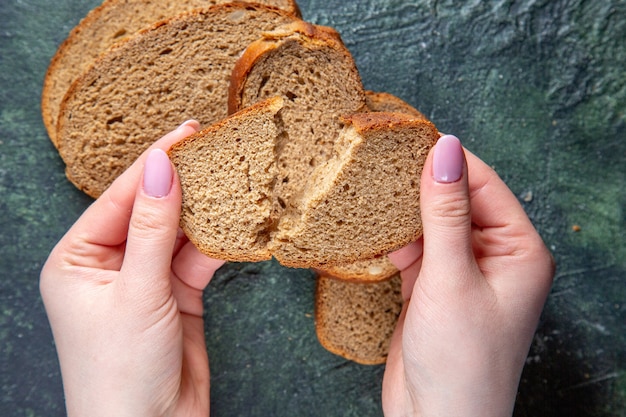 Top view dark bread loafs with female tearing on dark desk