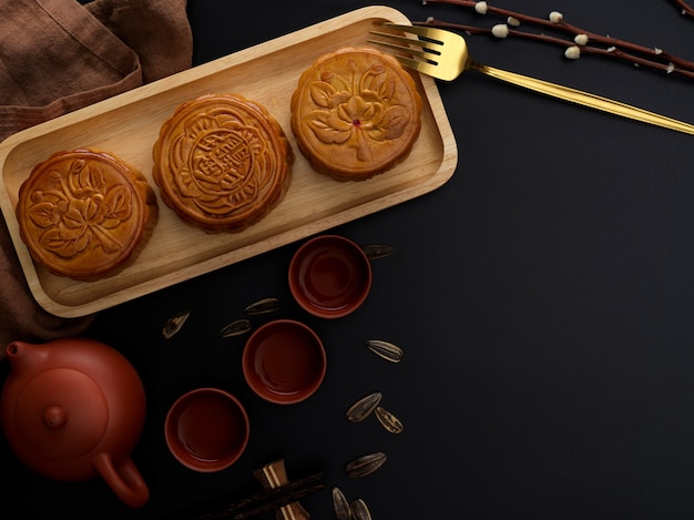 top view of dark modern table with tea set, moon cakes on wooden tray, decoration and copy space. chinese character on the moon cake represent "five kernel and roast pork" in english