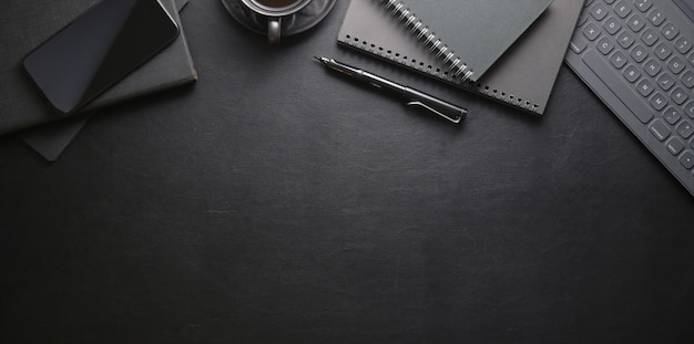 Top view of dark stylish workplace with smartphone and office supplies