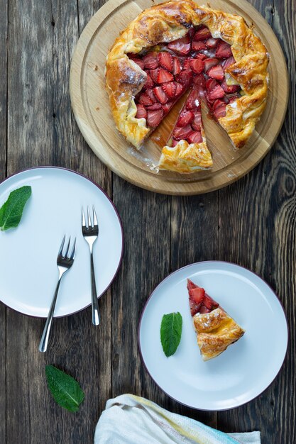 Top view of delicious baked tart with strawberries with plates and forks on a wooden table