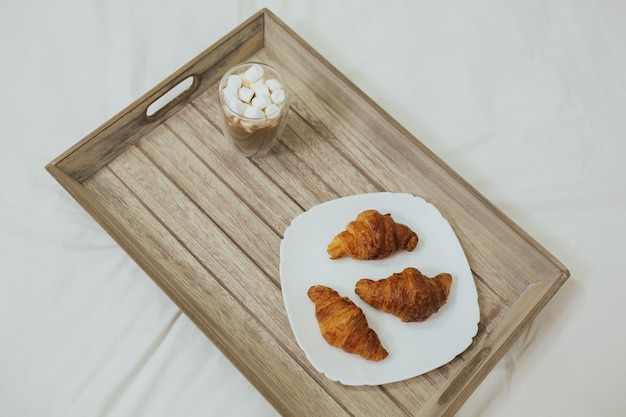 Vista dall'alto di una deliziosa colazione a letto con croissant appena sfornati con marmellata e caffè su un tavolo di legno