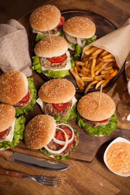 Top view of delicious burgers on wooden tablet next to chef knife. Food composition