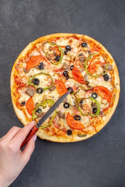 Vista dall'alto una deliziosa pizza al formaggio con olive, pepe e pomodori sulla superficie scura