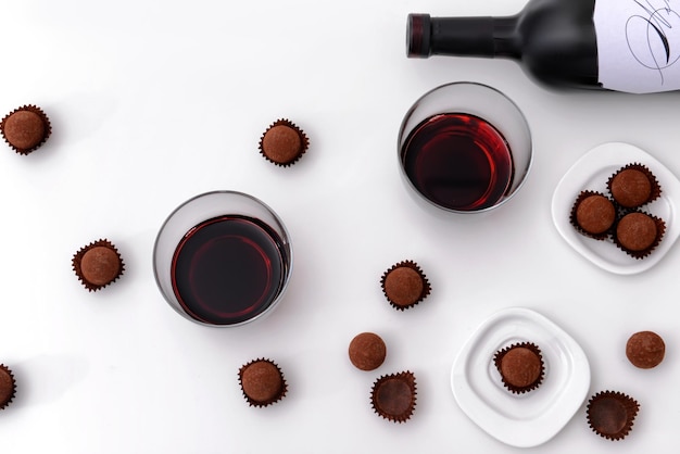 Top view of delicious chocolate truffles and red wine on white background