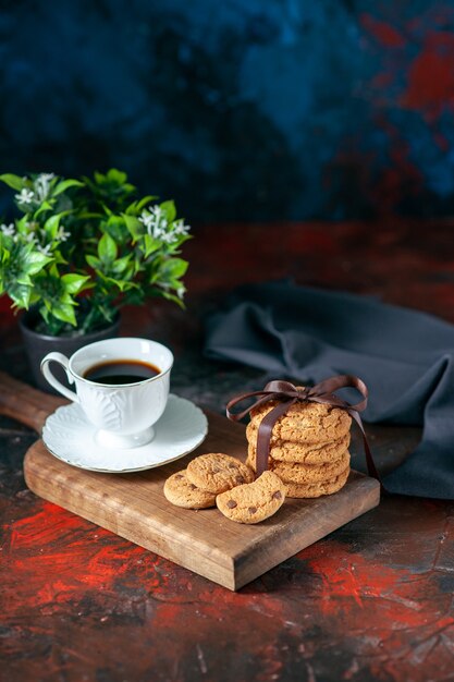 Foto vista dall'alto di un delizioso caffè in una tazza bianca e biscotti di zucchero fatti in casa su un vaso di fiori in legno marrone su sfondo di colori misti scuri con spazio libero