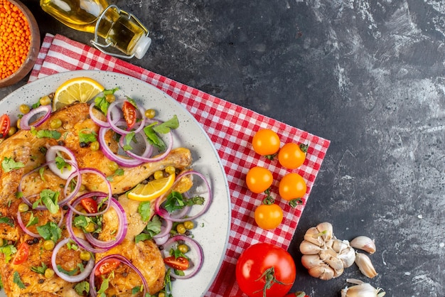 Top view of delicious dinner fried chicken dish with various spices and foods tomatoes with stems red lentil garlics fallen oil bottle lemon on the right side on dark color background