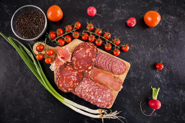 Вид сверху на вкусные здоровые мясные закуски на деревянной доске рядом с помидорами черри, редисом и зеленым луком