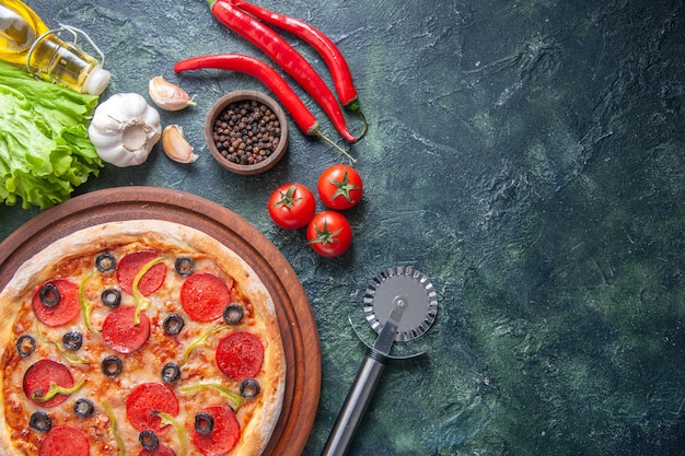 Top view of delicious homemade pizza on wooden cutting board tomatoes ketchup garlics pepper oil bottle green bundle on dark surface