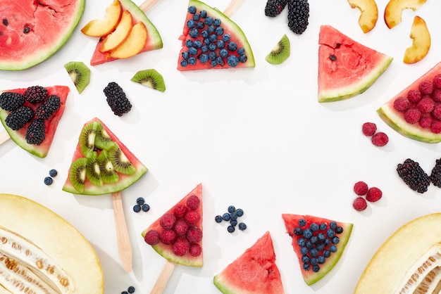 Top view of delicious juicy watermelon on sticks with seasonal berries and fruits on white