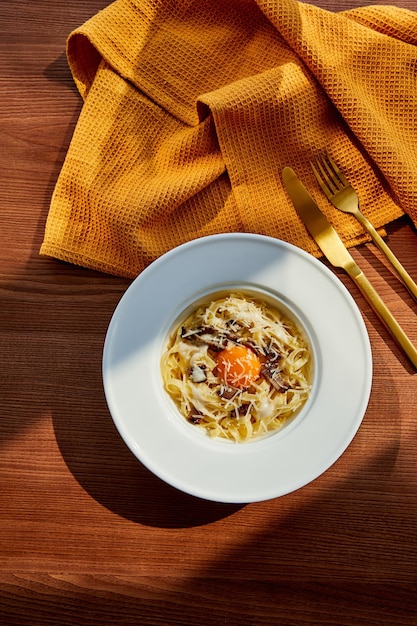 Top view of delicious pasta carbonara served with golden cutlery and yellow napkin on wooden table