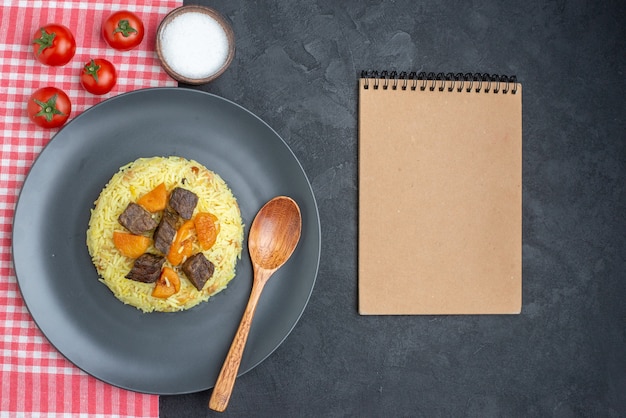 Top view delicious pilaf cooked rice with meat slices salt and tomatoes on dark surface