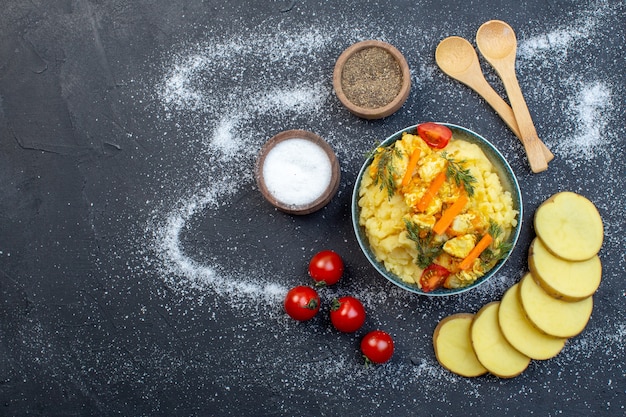 Top view of delicious potato meal with fresh vegetables spices spoons tomatoes on white black mixed color background with free space