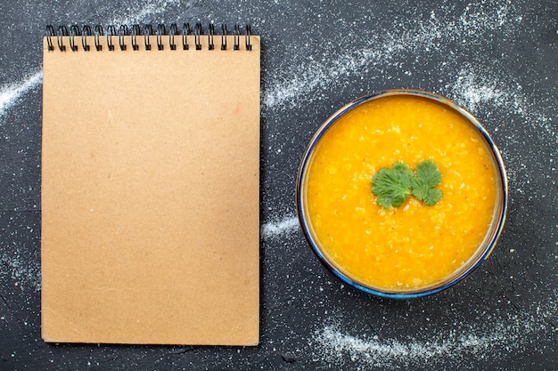 Top view of delicious red lentil soup in a bowl served with greens and spiral notebook on black white background with free space