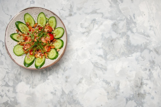 Top view of delicious salad decorated with chopped cucumber and greens on the right side on stained white surface