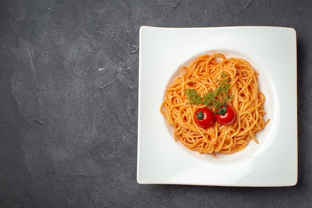 검정색 배경의 왼쪽에 있는 흰색 사각형 모양의 접시에 토마토 채소와 함께 제공되는 맛있는 스파게티의 상단 전망