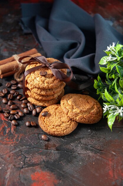 Foto vista dall'alto di deliziosi biscotti di zucchero e chicchi di caffè, vaso di fiori, cannella, lime, asciugamano su sfondo scuro di colori misti