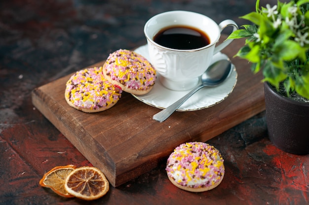 Vista dall'alto di deliziosi biscotti di zucchero e una tazza di caffè su tavola di legno vaso di fiori di limoni essiccati su sfondo scuro di colori misti