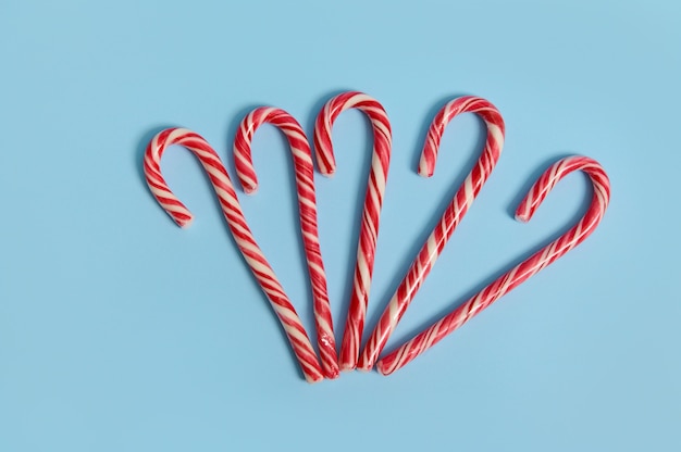 Top view of delicious sweet candy canes on blue background with copy space for Christmas advertising.