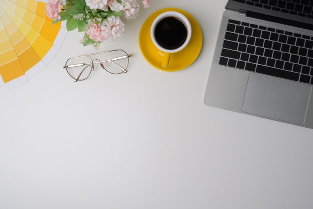 Top view designer workspace with laptop computer, coffee cup and glasses on white table.