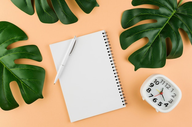 Top view of desk with notebook with leaves and clock