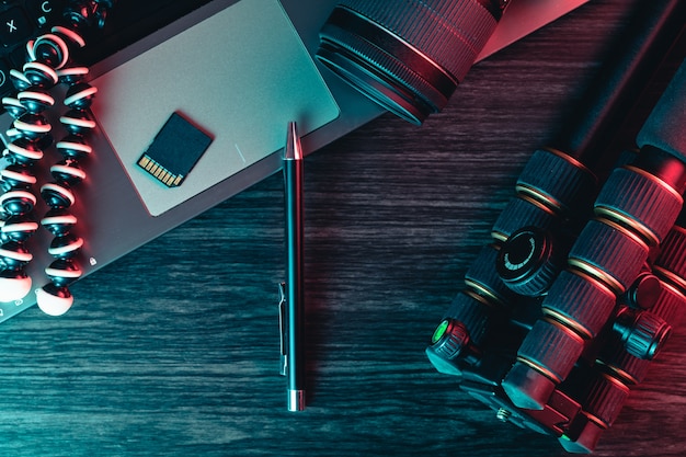 Top view of a desk working with laptop keyboard, modern camera, tripod and a pen