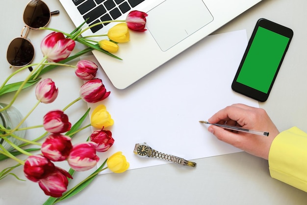 Photo top view of a desktop on which a woman's hand writes on a blank sheet of paper, copy space.