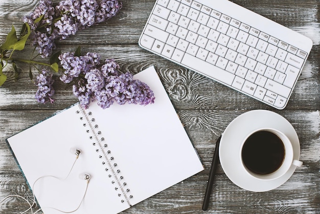 Top view of a diary, keyboard, headphones and a cup of coffee and a purple flower on a gray wooden table. Flat design.