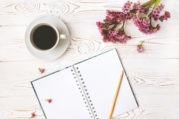 Top view of a diary or notebook, pencil and coffee and a purple flower on a white wooden table. Flat design.