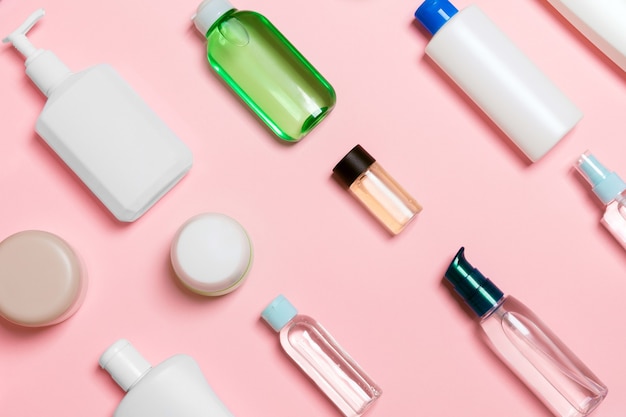 Top view of different cosmetic bottles and container for cosmetics on pink background. Flat lay composition with copy space.