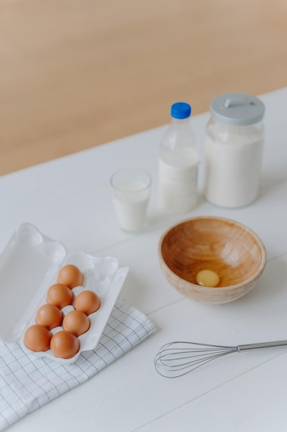 식탁에 있는 다양한 반죽 레시피 재료의 상위 뷰 계란은 우유와 밀가루 한 잔을 휘젓고 베이킹 및 요리 개념을 요리합니다