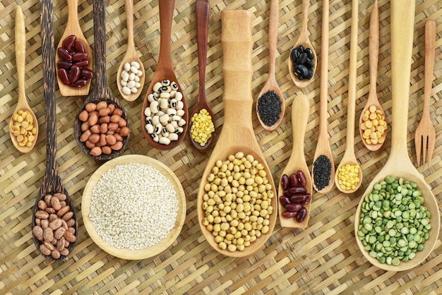 Top view different multicolour legumes in wooden spoon flat lay on bamboo woven