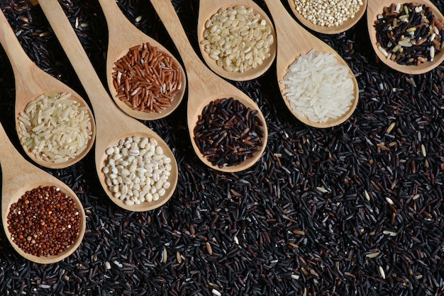 Вид сверху различные рис на деревянный совок с черным фоном рисового рисования, различные рис органических на деревянной ложкой коллекции