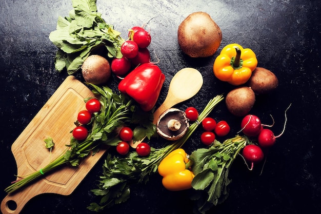 Over top view of different type of vegetables on dark board. Red and yellow pepper, mushrooms, cherry and greens