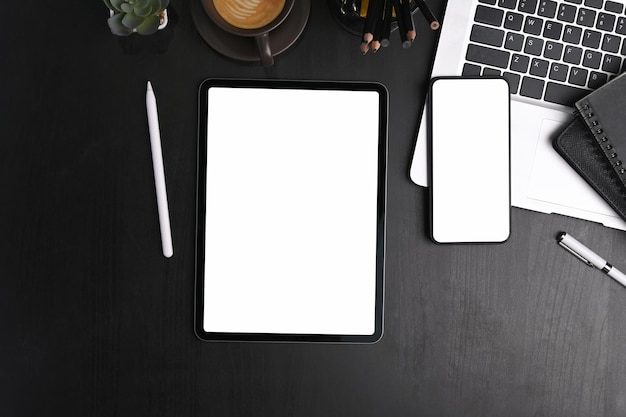 Top view of digital tablet, mobile phone, laptop computer and office supplies on black leather.