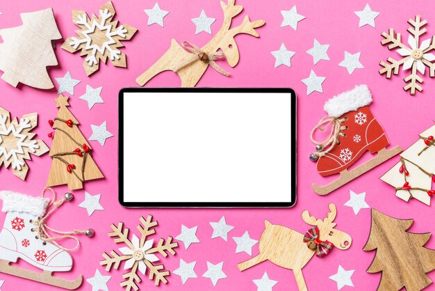 top view of digital tablet pink background decorated with festive toys and christmas symbols reindeers and new year trees holiday concept