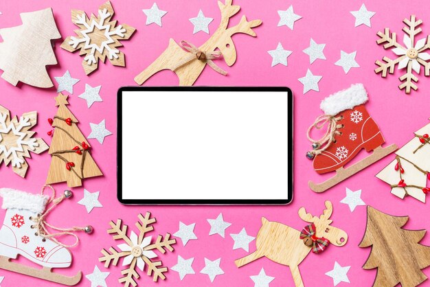 Photo top view of digital tablet pink background decorated with festive toys and christmas symbols reindeers and new year trees holiday concept