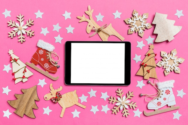 top view of digital tablet, pink decorated with festive toys and christmas symbols reindeers and new year trees