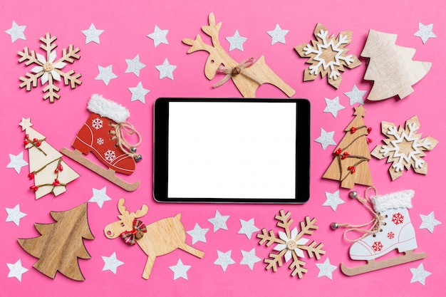 Top view of digital tablet, pink decorated with festive toys and Christmas symbols reindeers and New Year trees