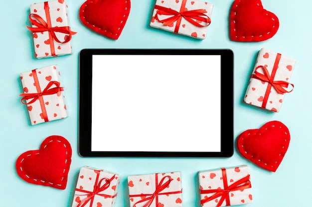 Top view of digital tablet surrounded with gift boxes and hearts on wood