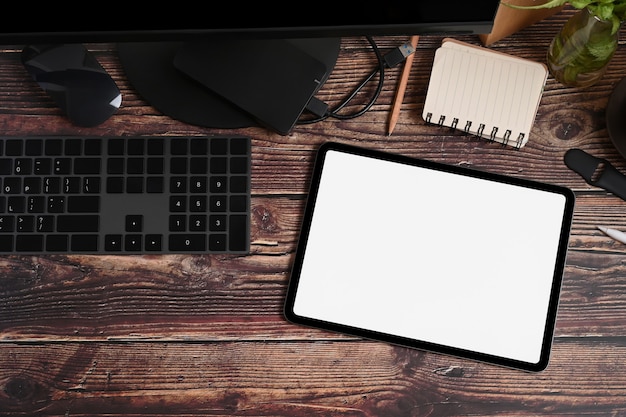 Top view digital tablet with empty screen and black equipment on wooden table.