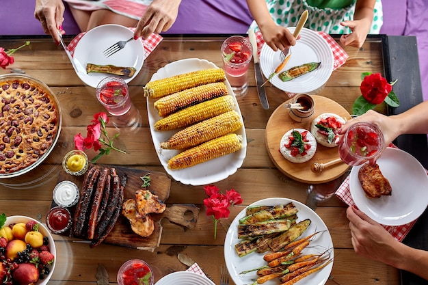 Top view over a dining table, decorated with flowers, with tableware and food. Backyard picnic with friends or neighbors, family dinner.