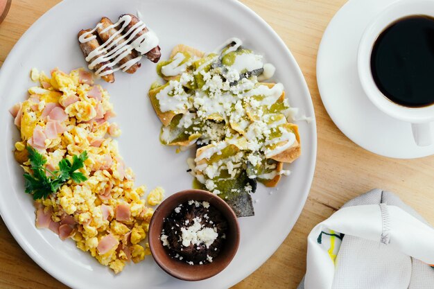 Top view of a dish with chilaquiles, egg, beans and a cup of coffee.