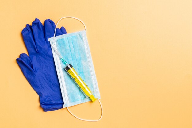 Top view of disposable surgical mask, pair of latex medical gloves and syringe on orange background. Virus protection concept with copy space