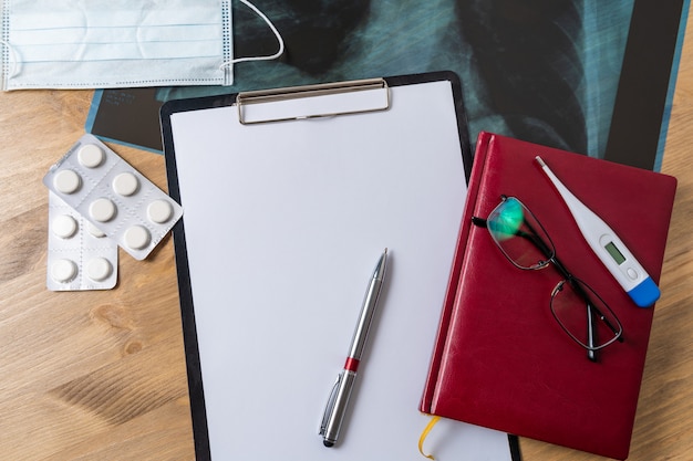 Top view of doctor's desk table, blank paper on clipboard with pen. Copy space.