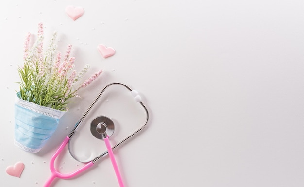 Top view of doctor stethoscope medical mask and flowers on white background International nurse day and medical concept