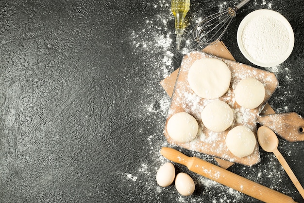 Top view dough balls on a wooden plate with cooking ingredients on the black background