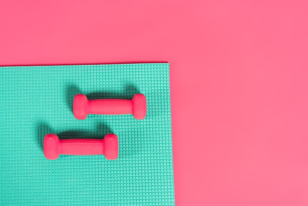 Top view of dumbbells on fitness mat isolated on pink