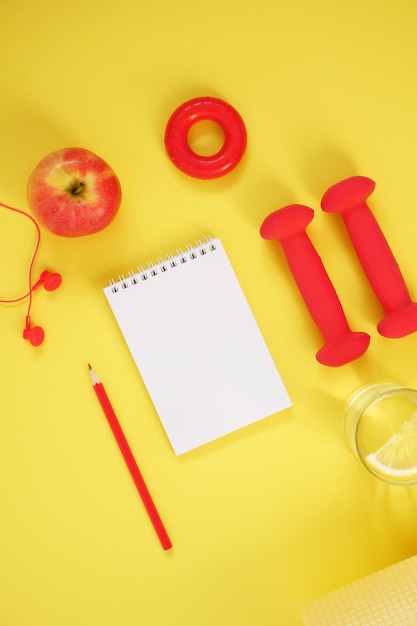 Top view of dumbbells headphones hand expander apple notebook and pencil on a yellow background